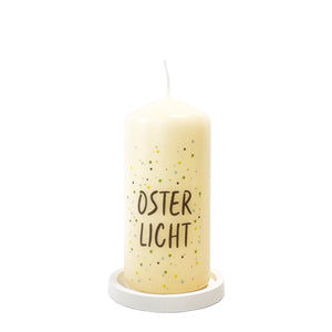Blockkerze mit flachem Kerzenteller aus Raysin. Kerze bedruckt mit Spruch: Osterlicht. Hintergrund Konfettidruck in blauen Tönen. Kerze zu Ostern